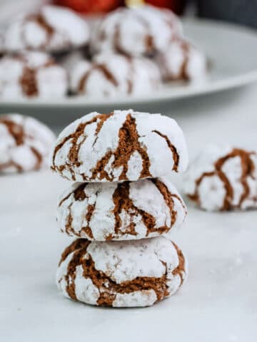 a stack of three chocolate crinkle cookies with a plateful in the background