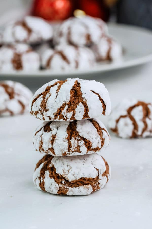 a stack of three chocolate crinkle cookies with a plateful in the background