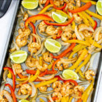 a baking sheet full of shrimp, red and orange peppers and lime slices