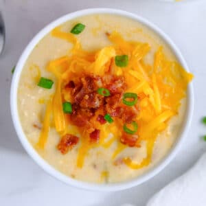 closeup of baked potato soup topped with shredded cheese, bacon and scallions