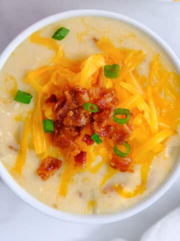 closeup of baked potato soup topped with shredded cheese, bacon and scallions