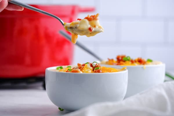 a white bowl with potato soup and a spoon with soup on it