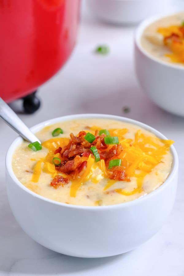 a white bowl with potato soup with cheese, bacon and scallions on top