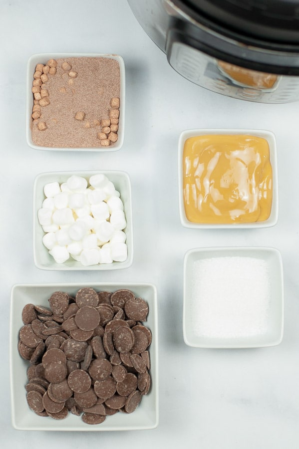 several white bowls with chocolate, mini marshmallows, cocoa powder, caramel, and salt