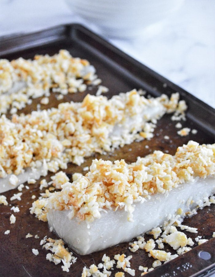 raw cod fillets on a baking sheet topped with breadcrumb topping