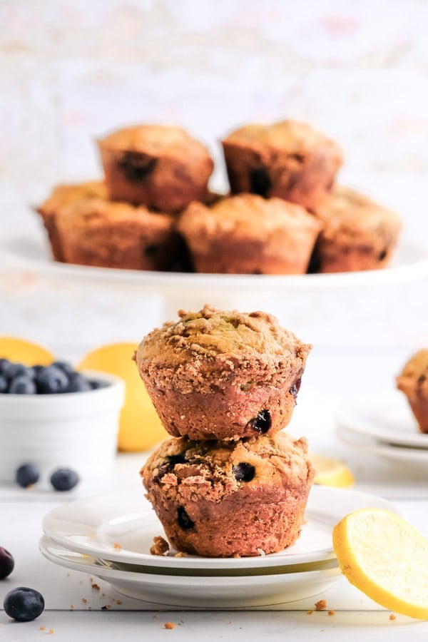 two lemon blueberry muffins stacked with a stand full of muffins in the background