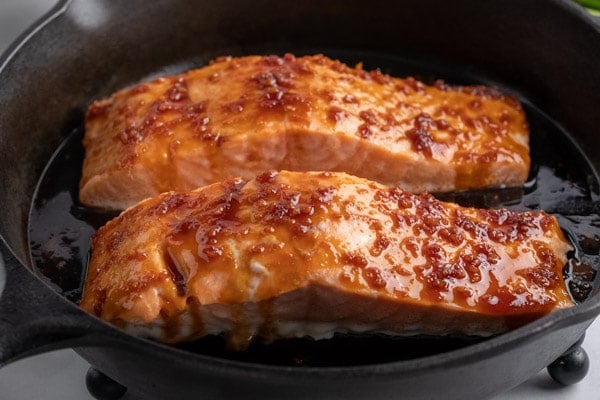 two salmon fillets in a cast iron pan topped with maple soy sauce