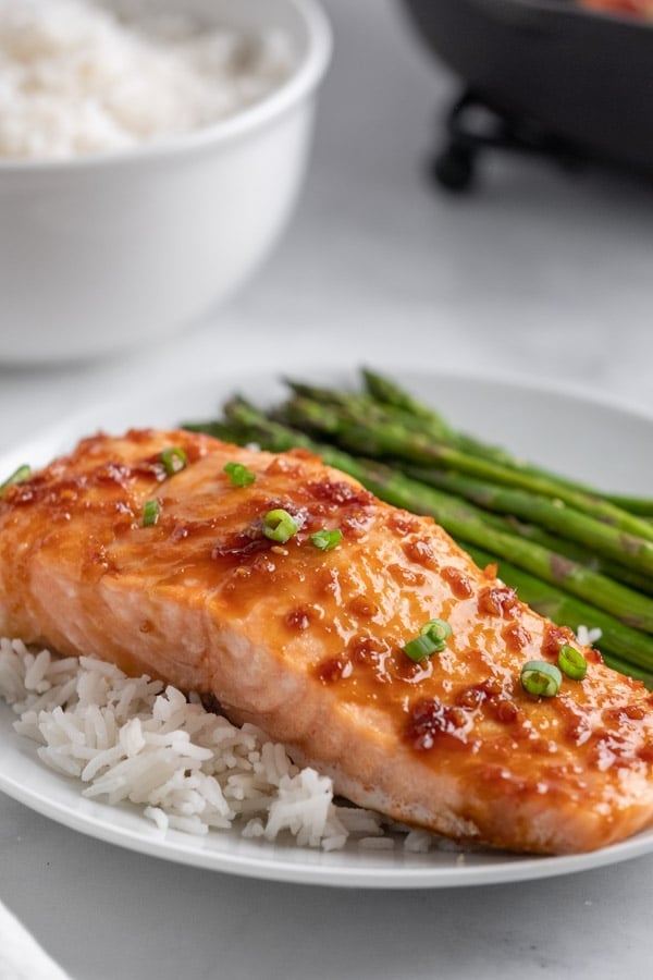 salmon fillet topped with chives and soy maple glaze on a plate with rice and asparagus