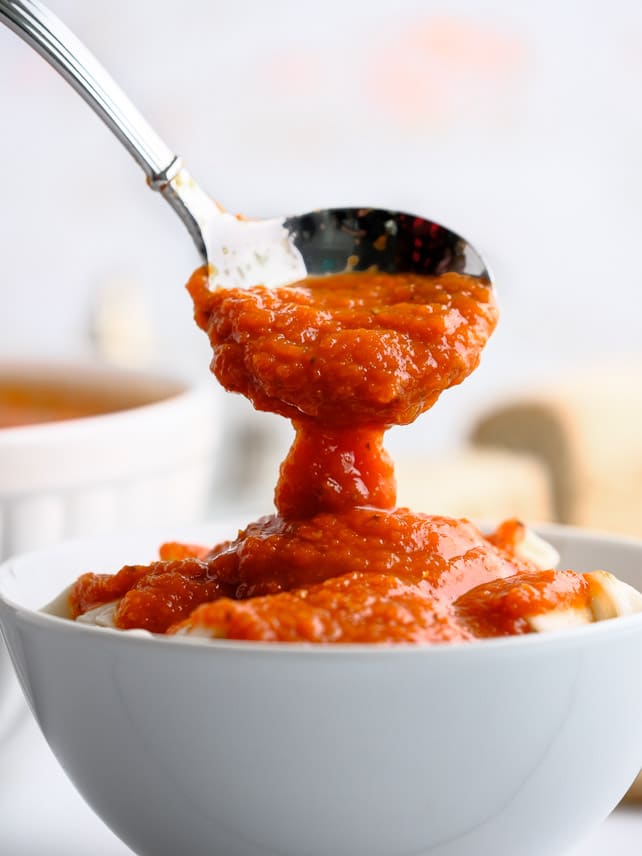 marinara sauce being poured onto pasta in a white bowl