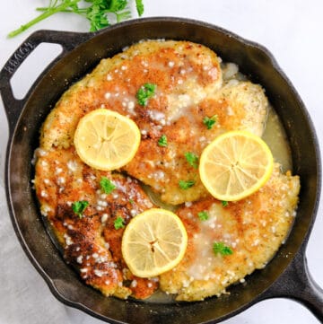 four breaded chicken breasts in a cast iron skillet with lemon slices