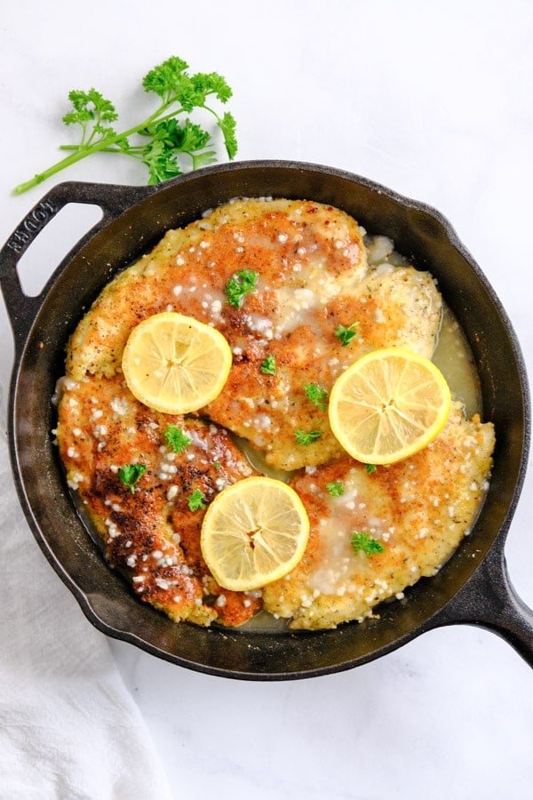 four breaded chicken breasts in a cast iron skillet with lemon slices