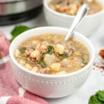 sausage potato spinach soup in a white bowl with a spoon