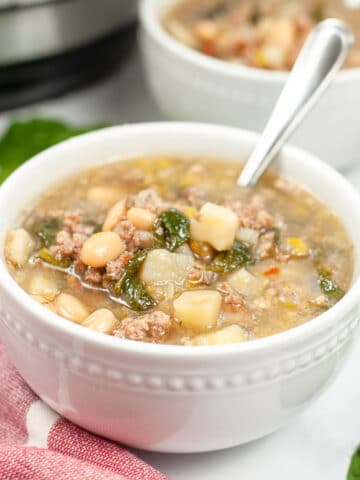 sausage potato spinach soup in a white bowl with a spoon