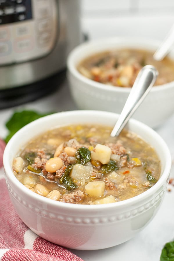 sausage potato spinach soup in a white bowl with a spoon