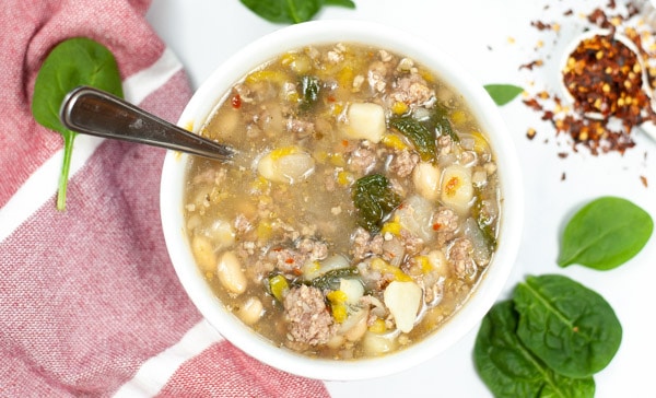 sausage potato and spinach soup with surrounded by a red napkin and spinach