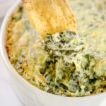 spinach artichoke dip being scooped out of a dish