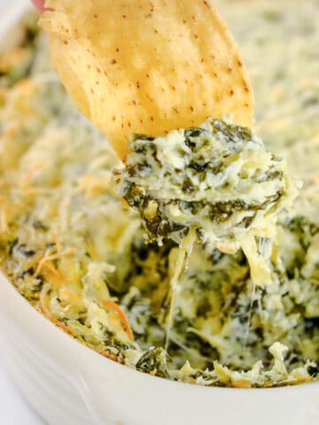 spinach artichoke dip being scooped out of a dish