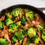 a cast iron skillet with beef strips and broccoli covered in a brown sauce