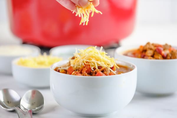 closeup of a bowl of chili being sprinkled with shredded cheese