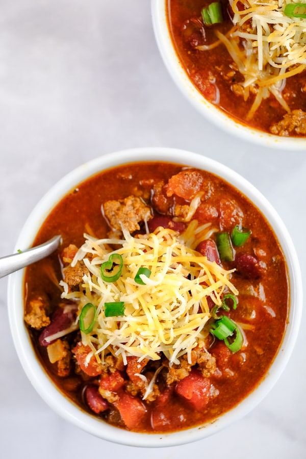 a bowl full of beef chili in a white bowl topped with cheese and chives