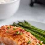 a salmon fillet topped with soy glaze over white rice with asparagus on a white plate