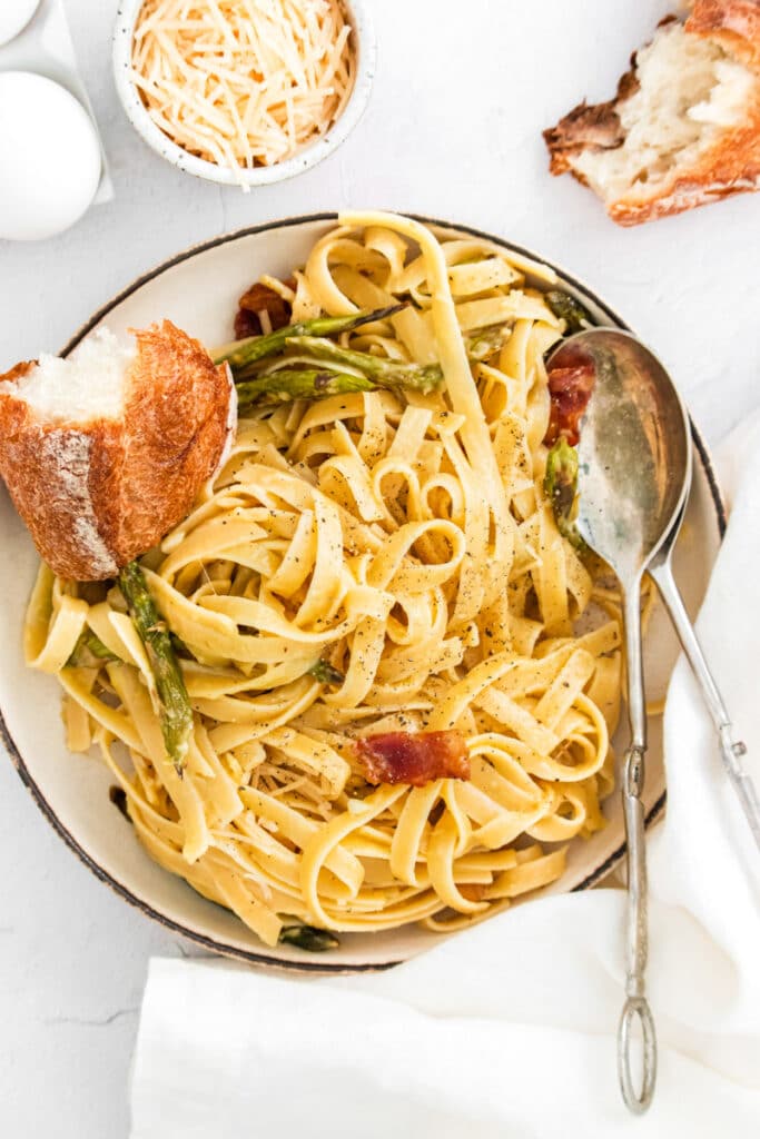 closeup of fettuccine noodles with asparagus and bacon with a spoon and bread