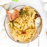 closeup of fettuccine with asparagus and bacon in a bowl with bread and spoon