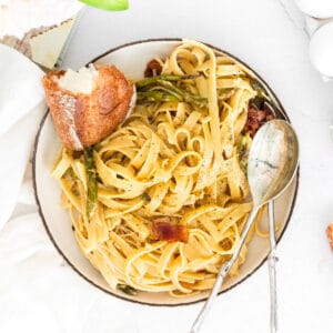 closeup of fettuccine with asparagus and bacon in a bowl with bread and spoon