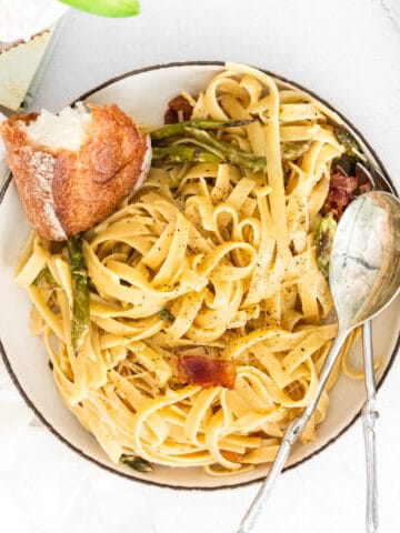 closeup of fettuccine with asparagus and bacon in a bowl with bread and spoon