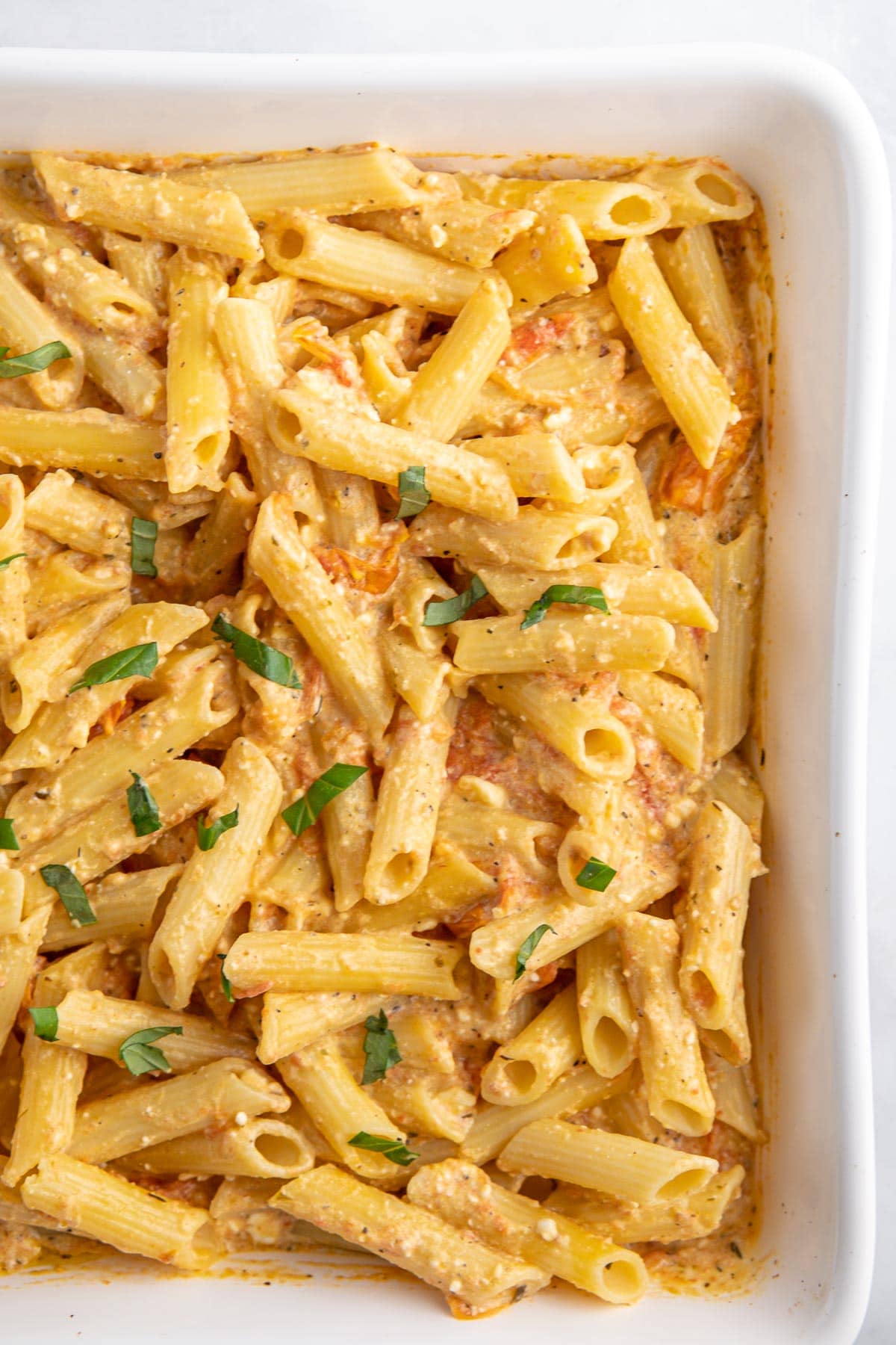 a white baking dish with penne pasta in a feta cream sauce.