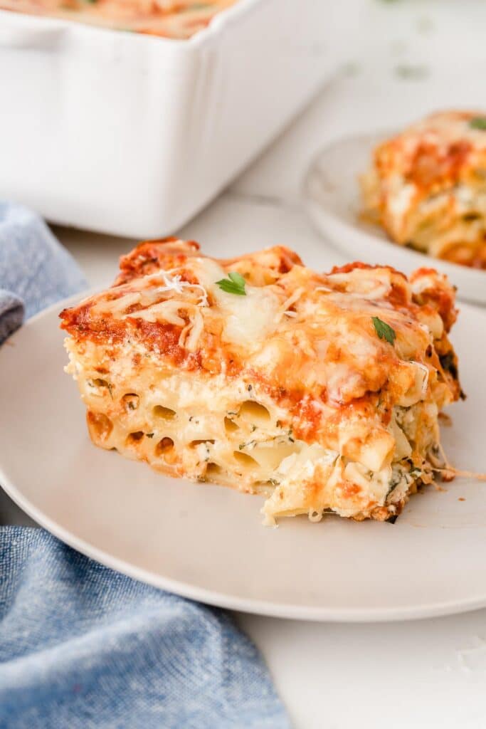 closeup of a slice of baked ziti on a white plate with a light blue napkin