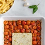 white square baking dish with cherry tomatoes surrounding a block of feta cheese