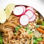 closeup of rice noodles toped with peanuts, radish slices, sliced carrots and green onions