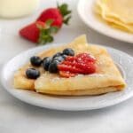 two homemade crepes folded and topped with blueberries and sliced strawberry