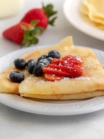 two homemade crepes folded and topped with blueberries and sliced strawberry
