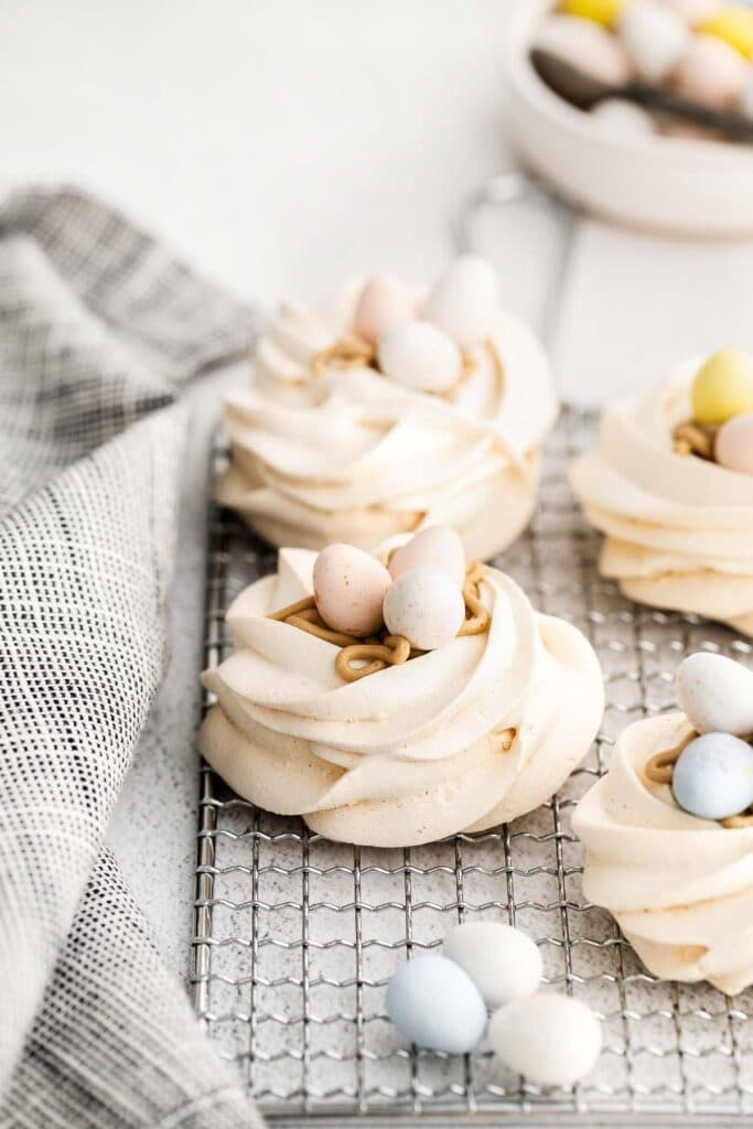 closeup of meringue nests on a wire rack with easter cadbury egg candy on top