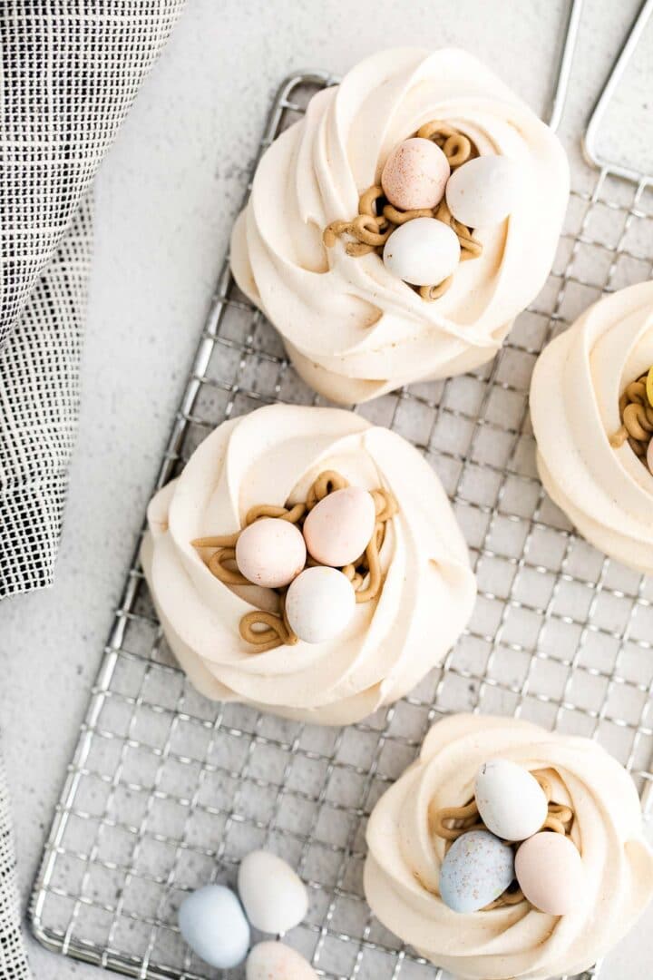 four meringue nests on a silver wire rack with eggs on top