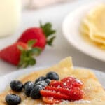 two folded crepes topped iwth strawberries and blueberries on a white plate