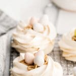 three meringue nests on a wire rack topped with chocolate pastel eggs
