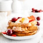 four slices of brioche french toast with slices of banana, cherries, strawberries and powdered sugar