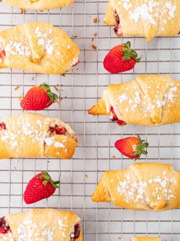 several crescent rolls on a wire cooling rack with fresh strwberries