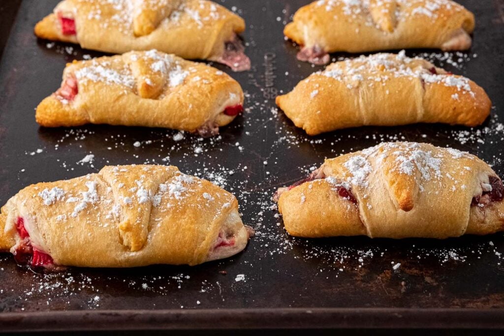 a baking sheet with six crescent rolls sprinkled with powdered sugar