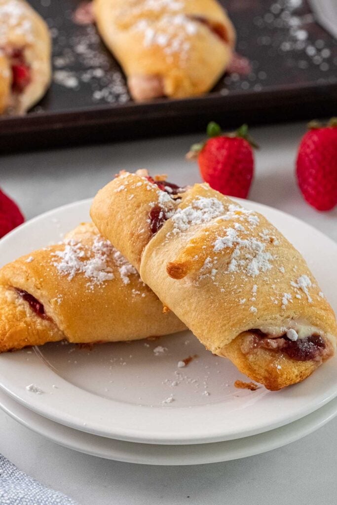 two crescent rolls topped with powdered sugar leaning on each other on a white plate