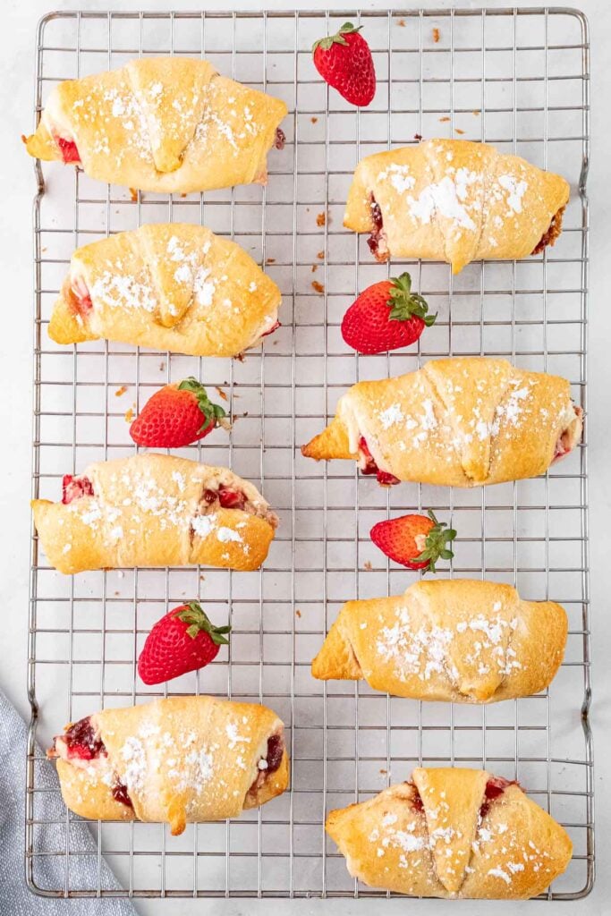 eight crescent rolls filled with strawberry cream cheese mixture and topped with powdered sugar on a wire rack