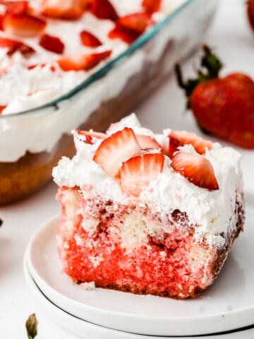 closeup of a square slice of strawberry poke cake topped with fresh strawberries on a white plate
