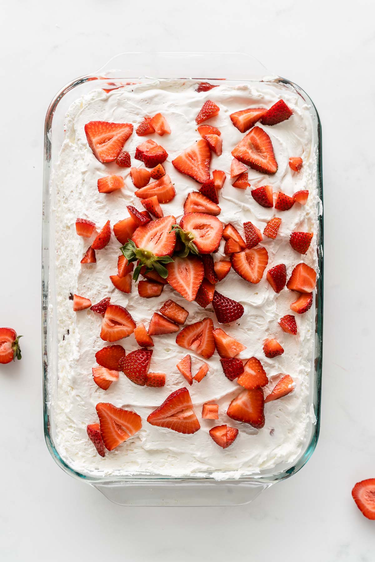 strawberry poke cake topped with whipped cream and fresh strawberry slices in a 9x13 glass baking dish