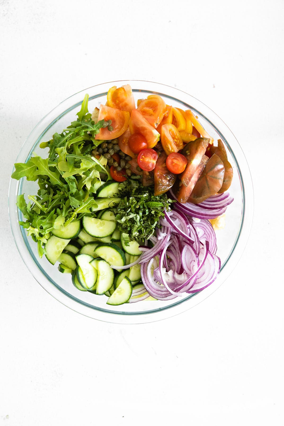 glass bowl with arugula, sliced cucumbers, sliced red onions, and tomatoes