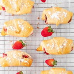 eight crescent rolls filled with strawberry cream cheese mixture and topped with powdered sugar on a wire rack with text overlay