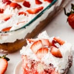 piece of strawberry poke cake on a white plate with a 9x13 glass dish full of cake and text overlay that reads strawberry poke cake