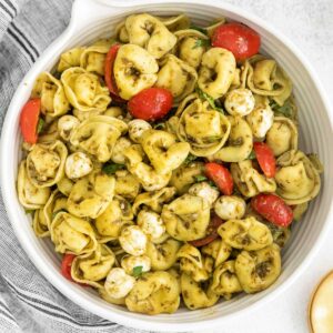 white bowl with tortellini pasta salad with tomatoes and pesto sauce
